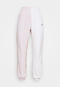 Nike sweatpants with a patchwork design in light pink, white, and tan, featuring elastic cuffs and waistband. Minimalistic branding on the front.