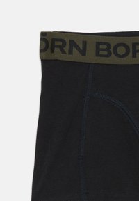 Sorte boxerbriefs med mørke olivengrønne taljer, der har stor sort delvis tekst og synlige sømdetaljer på stoffet.