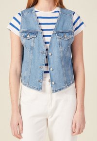 Jasnoniebieska denimowa kamizelka z dwiema kieszeniami na piersi, zapięciem na guziki i surowym wykończeniem. Nosi się ją na białej koszulce w niebieskie paski. Prosty design.