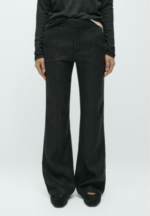 Pantaloni neri a gamba larga realizzati in tessuto morbido con una texture liscia, caratterizzati da una vita alta e cuciture visibili sul davanti.