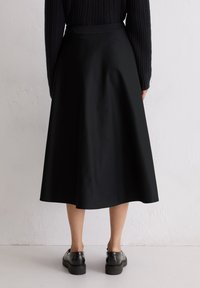 Jupe midi noire en forme A avec une texture lisse et une couleur unie, dotée d'une taille ajustée et d'un ourlet évasé. Portée avec des chaussures noires.