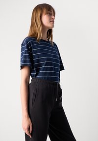 Marine stripete T-skjorte med korte ermer og rund hals, kombinert med svarte joggebukser med snøring. Uformelt og komfortabelt design.