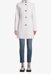 Abrigo gris claro con un alto cuello, botones en la parte delantera y bolsillos en las costuras laterales, combinado con unos jeans azules y botas de tobillo de encaje color crema.