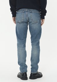 Svetlo modri kavbojke v ožjem kroju, z obliko petih žepov, subtilnim bledenjem in detajli šivanja, v kombinaciji s črnimi usnjenimi škornji.