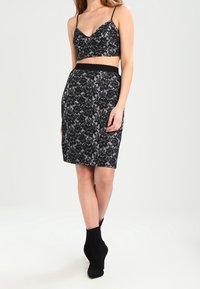 Černý krajkový crop top s tenkými ramínky v kombinaci s přiléhavou černou krajkovou tužkovou sukní. Obsahuje květinové vzory a texturovaný povrch.