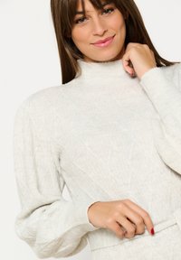 Light gray knitted sweater with a high neck, textured pattern, puffed sleeves, and ribbed cuffs. Soft material and fitted silhouette.