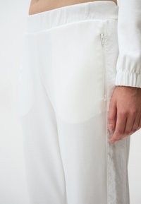 Witte joggingbroek gemaakt van zacht materiaal, met een gladde elastische tailleband en een zijzak met rits, met een recht pijpdesign en zonder patronen.