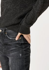 Czarny sweter o teksturowanej powierzchni z prążkowanym wzorem. Połączony z ciemnoszarymi dżinsami z przetarciami i widocznymi szwami przy kieszeni.