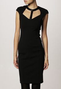 Robe noire ajustée avec des manches courtes, présentant un décolleté en découpe et un détail de col brillant. Texture lisse, design jusqu'aux genoux.