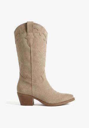 Botte de cowboy beige en daim mi-mollet avec des coutures décoratives, un bout pointu et un talon bloc empilé.