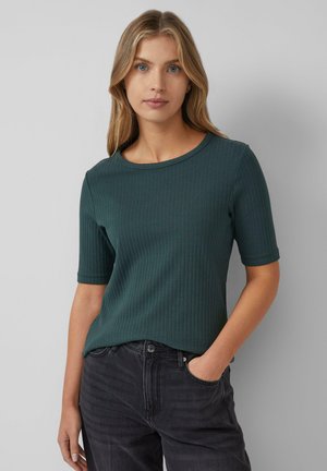 Haut à manches courtes en ribbed vert foncé avec un col rond, offrant un design ajusté et une texture subtile, associé à un jean foncé.