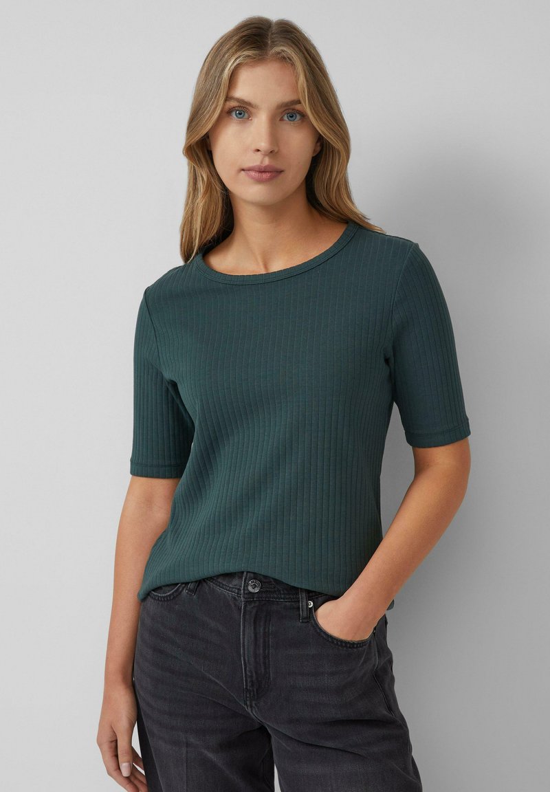 Maglietta a maniche corte a coste verde scuro con scollatura rotonda, caratterizzata da un design attillato e una texture sottile, abbinata a jeans scuri.