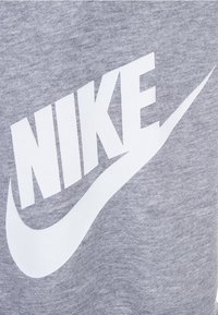 Šedá tkanina s výrazným bílým logem Nike a znakem swoosh, hladká textura a ležérní design vhodný pro sportovní oblečení.