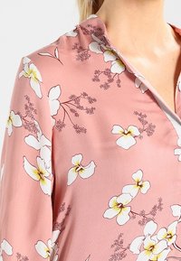 Rosa blus med blommönster i vitt och gult. Slät tyg med krage och korta ärmar.