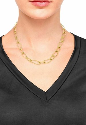 Goldene Kettenhalskette mit verlängerten, verdrehten Gliedern. Getragen über einem schwarzen V-Ausschnitt-Oberteil, das die glatte Textur und den Glanz hervorhebt.