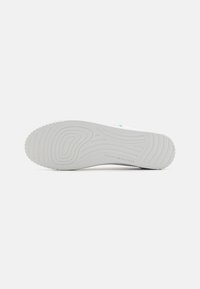 Talpa de sneaker albă cu un model de cauciuc texturat. Prezintă detalii subtile cu logo și elemente de tracțiune circulare pentru aderență.