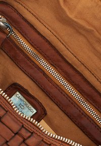 Interno di una borsa in pelle intrecciata marrone, con cerniera argentata e fodera in tessuto beige, con un'etichetta del marchio visibile.