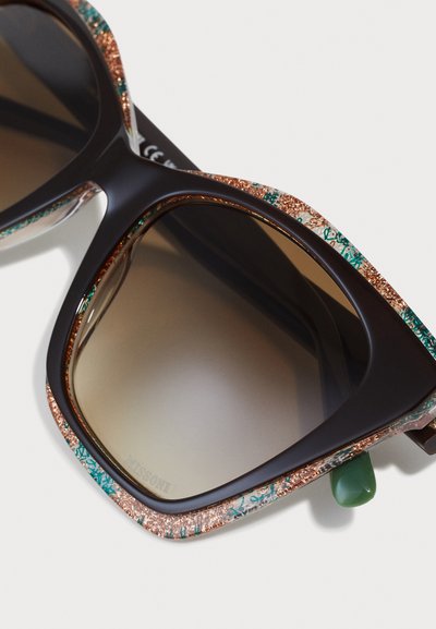 Braune overgroße Sonnenbrille mit einem gemusterten, glitzernden Rahmen in Türkis und Kupferakzenten. Enthält ein grünes Detail am Bügel.