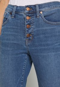 Džínové kalhoty s vysokým pasem v modré barvě, s knoflíkovým zapínáním, obsahující pět kovových knoflíků a prošití, s hladkou texturou středního praní.