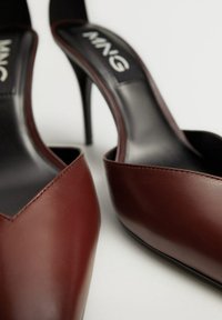 Chaussures à talons hauts en cuir marron foncé avec bout pointu et dos ouvert, dotées d'un design élégant et d'une semelle intérieure noire avec marquage blanc.