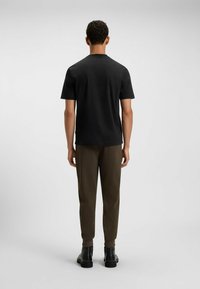 Czarna koszula z krótkim rękawem i okrągłym dekoltem, w połączeniu z oliwkowo-zielonymi spodniami o tapered cut i czarnymi botkami za kostkę, widok z tyłu.