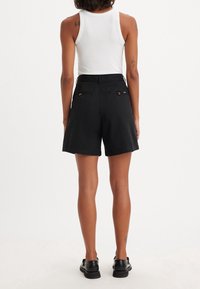 Shorts noirs taille haute avec une coupe ample. Confectionnés dans un tissu texturé, ils présentent des poches arrière avec des boutons en accent et des bords ourlés.
