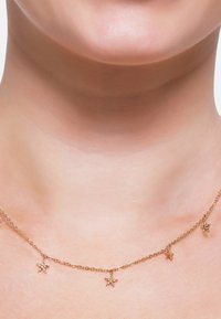 Collier en chaîne dorée avec de petits charms en forme d'étoile, des maillons délicats et une texture lisse, reposant sur un teint de peau neutre.