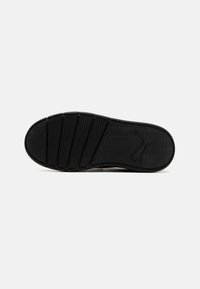 Semelle de chaussure de sport noire avec surface texturée et rainures horizontales. Présente un logo et un design plat et robuste pour une meilleure adhérence.