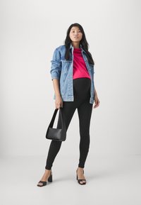 Denimjack, felroze top, zwarte leggings en zwarte hoge hak sandalen. Het model houdt een kleine zwarte handtas vast. Eenvoudige, moderne outfit.
