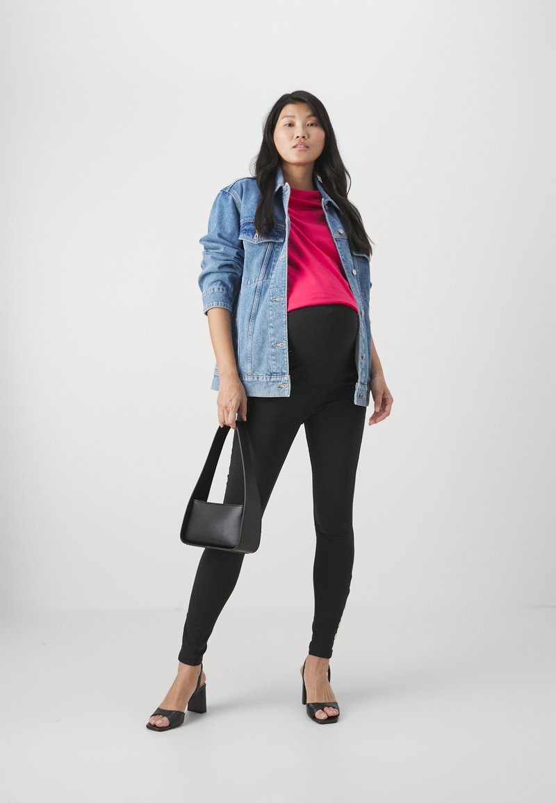 Denim jacket, bright pink top, black leggings, and black heeled sandals. The model holds a small black handbag. Simple, modern outfit.
