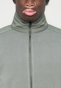 Gray zip-up jacket featuring a textured body, smooth collar, and shoulder accents. The fabric appears soft with a fitted design.