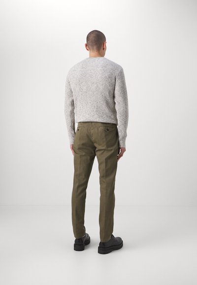 Grijze geribbelde trui, olijfgroene broek met voorzakken en zwarte schoenen. De outfit heeft een relaxte pasvorm en een gestructureerde stof.