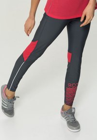 Czarne legginsy sportowe z czerwonymi akcentami z siateczki i wzorem w zygzak. Posiadają odblaskowy pasek wzdłuż boku. W połączeniu z szarymi trampkami.