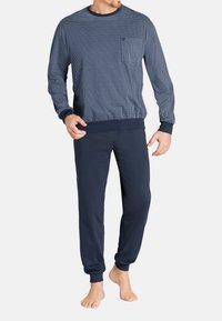 Navyblaues Loungewear-Set, bestehend aus einem gestreiften Langarmoberteil mit Rundhalsausschnitt und einer kleinen Tasche, kombiniert mit einfarbigen navyblauen Jogginghosen.