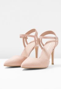 Nude mokasini korkokengät, joissa on terävä kärki ja nilkkaremmitys, varustettuna pienellä hopeisella soljella ja ohuella niittikorkealla.