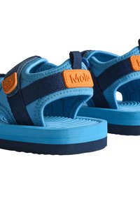 Zili sandaļi ar biezām, strukturētām zoles; ar tumši ziliem siksnām un oranžu Molo loga etiķeti. Materiāli ietver mīkstu audumu un gumiju.