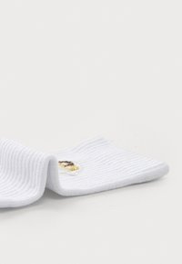 White ribbed sock featuring an embroidered design with gold accents. Soft texture with a folded tip, designed for comfort and fit.