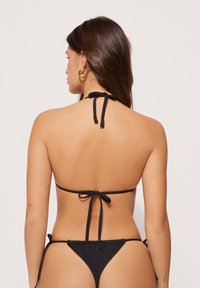 Bikini nero con design a collo alto, caratterizzato da sottili lacci al collo e sulla schiena, copertura minima e una texture di tessuto morbido e elasticizzato.