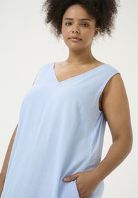 Hellblaues ärmelloses Kleid mit V-Ausschnitt, aus weichem Material gefertigt. Verfügt über Seitentaschen und einen lässigen Schnitt, der einfache Linien und minimale Akzente zeigt.