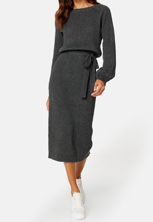 Woman wearing a dark gray ribbed knit sweater dress with long sleeves, waist tie, and white high-top sneakers, against a plain background.