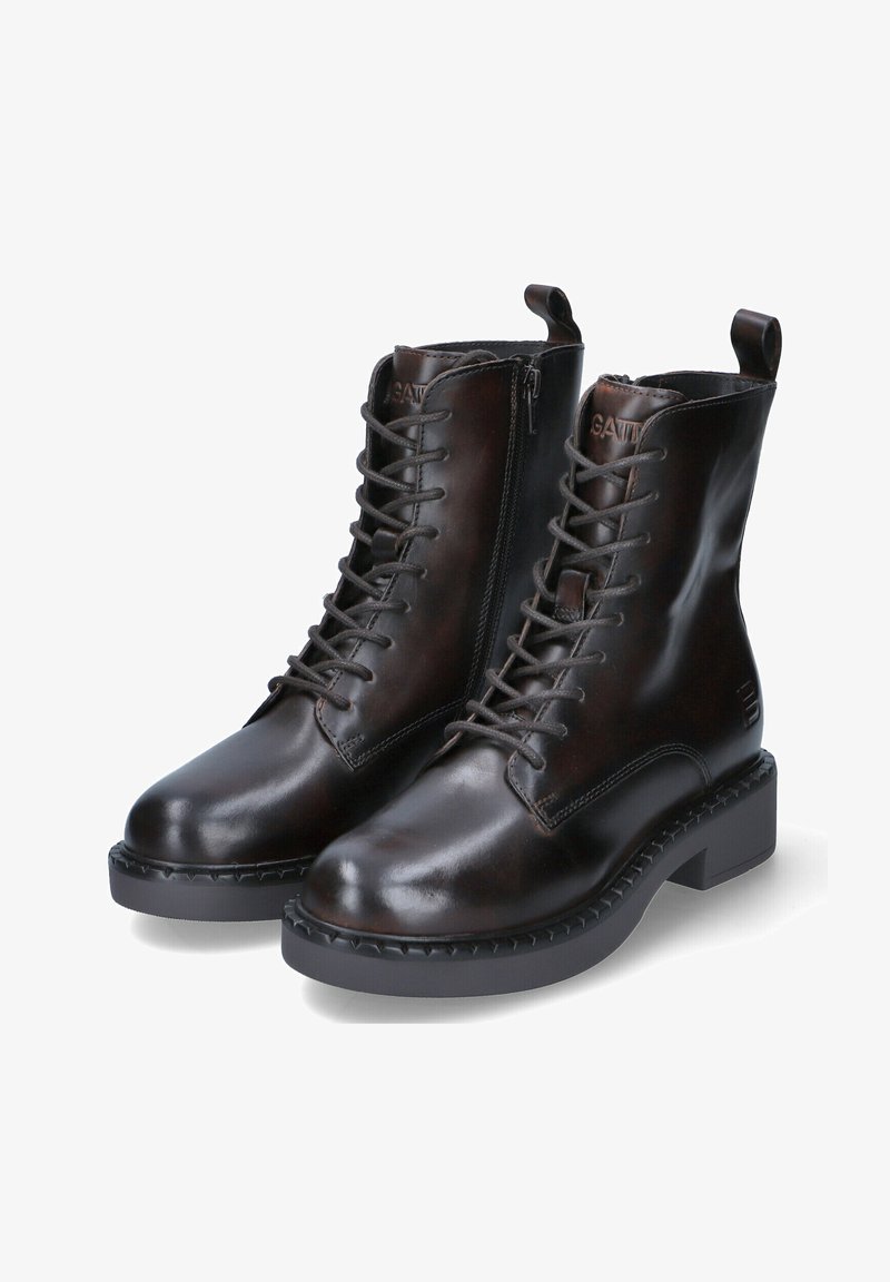 Bottes chevilles en cuir marron avec un laçage, bouts ronds et fermeture éclair sur le côté. Les semelles en caoutchouc noir épais et texturé ajoutent de la stabilité.