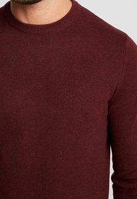 Bordeauxrode gebreide trui met een ronde hals en geribbelde boorden, met een gladde textuur en een aansluitend ontwerp.