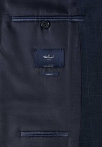 Vue intérieure d'une veste de costume bleu marine foncé montrant l'étiquette MNG sur mesure, l'étiquette slim fit, le bouton et les poches intérieures.