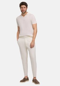 Lichte crème polo met V-hals en korte mouwen, gecombineerd met smalle witte broeken en bruine instapschoenen.