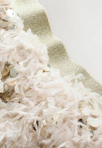 Struktureret stof i blød beige med pailletter og en bølgende gul accent. Indeholder en blanding af fluffy fibre og glatte metalelementer.