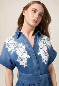 Denim jurk met korte mouwen, v-hals, witte bloemenborduursels op de schouders, gecinchede taille met bijpassende riem, zachte textuur, blauwe kleur.