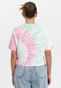 Gekropte tie-dye t-shirt met pastelroze en groene kleuren, voorzien van een cirkelvormig embleemontwerp op de achterkant. Korte mouwen en gemaakt van katoen.