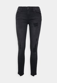 Pantalones vaqueros negros ajustados de denim, con un diseño desgastado que presenta roturas y deshilachado en el dobladillo. Ajuste slim con el estilo típico de cinco bolsillos.