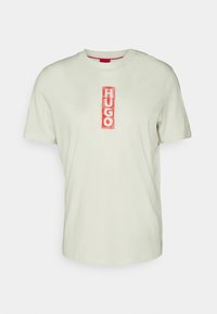 Světle zelené bavlněné tričko s kulatým výstřihem a krátkými rukávy. Uprostřed se nachází červené vertikální logo "HUGO". Hladký povrch.