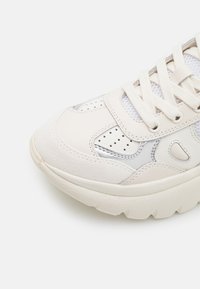 Vit sportskor med en kombination av slät läder, mocka och mesh-texturer med silverdetaljer, rund tå och vadderad sula.